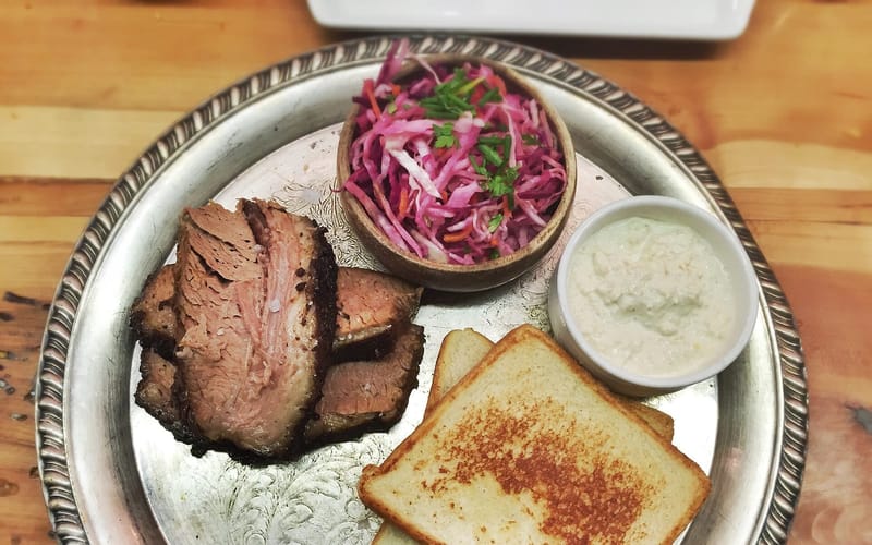 A tray of sliced smoked brisket with white bread and slaw