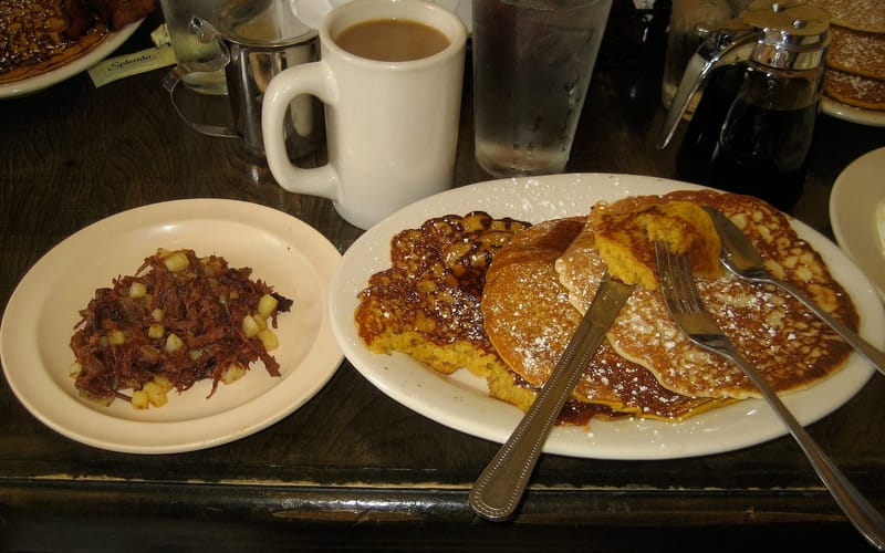 A breakfast plate of pancakes with a side of hash