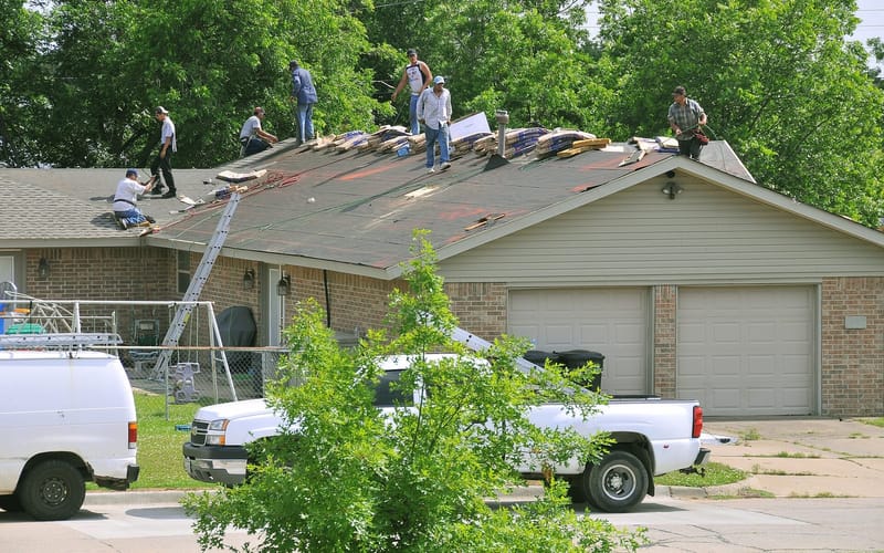 A roofing crew replacing asphalt shingles on a house