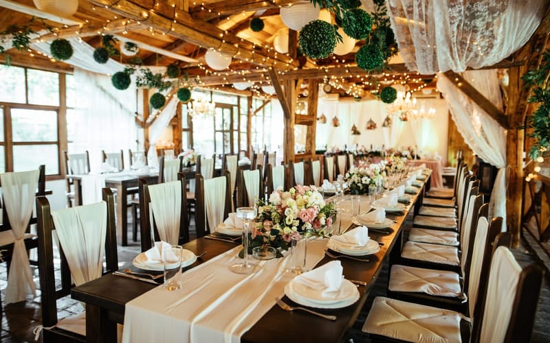 A barn wedding reception set with long tables, white linens and hanging lights