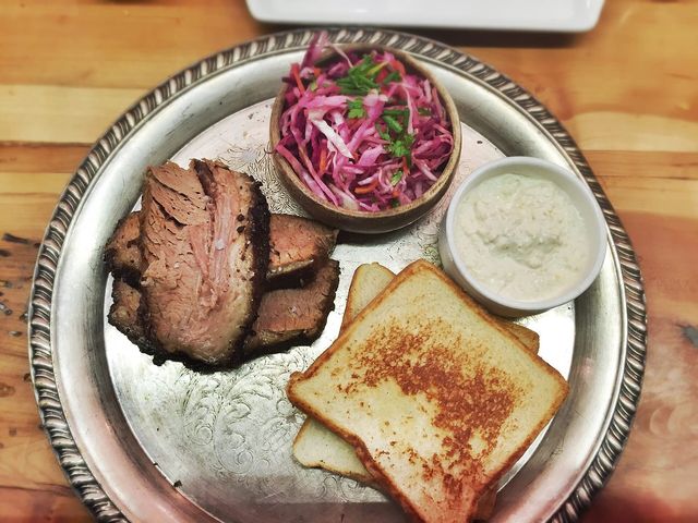 A tray of sliced smoked brisket with white bread and slaw