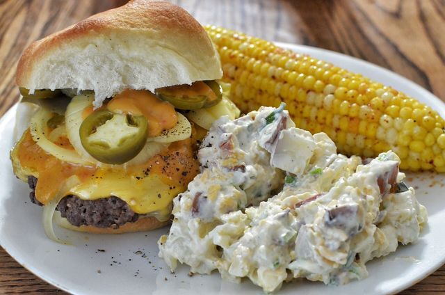 A cheeseburger served with potato salad and sweet corn