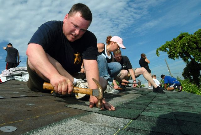 A worker nailing shingles onto the roof of a house