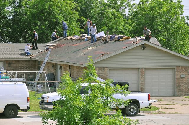 A roofing crew replacing asphalt shingles on a house